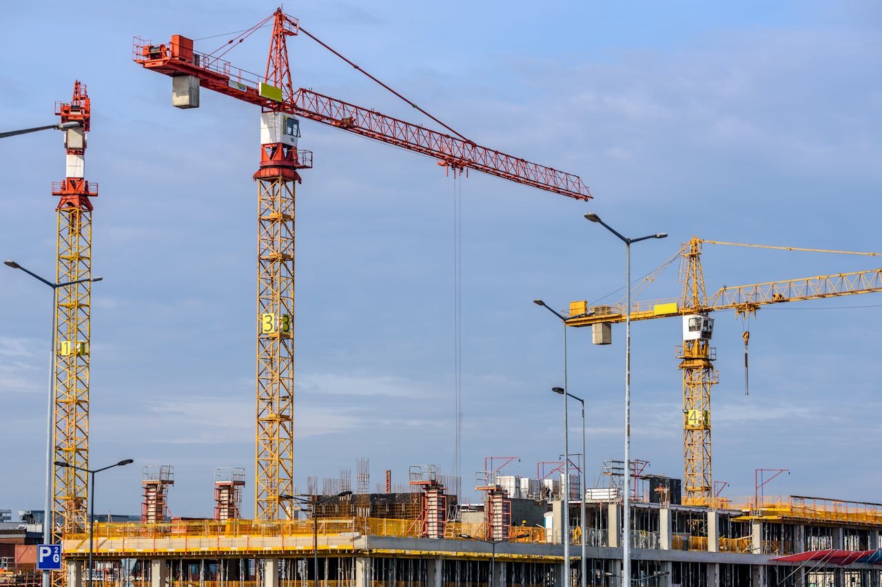 about-03 Multiple tower cranes working on a large construction site with blue sky backdrop.